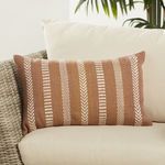 Lumbar pillow styled on beige cushioned outdoor wicker sofa with tropical plant in background