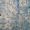 Close-up showing the distressed pattern and texture of the light blue and ivory rug with stacked books at top left