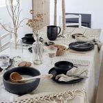 Multiple Pacifica bowls and plates on a linen-covered dining table with wooden and glass decor accents