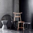 Benji Stool stacked with other stools and furniture pieces against a concrete wall with a round mirror
