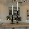 Lit white taper candles in Foundation Candleholders on wooden table with art and chandelier backdrop