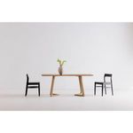 Dining table flanked by two black chairs with vase centered on top in open white space
