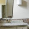 Single French Cuff Sconce mounted on wall over striped beige tile with light taupe vanity and scalloped mirror