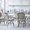 Rossini rattan dining armchairs with armrests viewed from back around white dining table with decorative plates