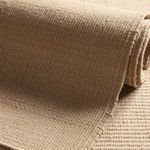 Rolled section of rug showing thickness and dense woven pile in solid tan color
