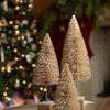 Cream bottle brush trees styled on a table with blurred Christmas tree and stockings in background