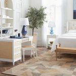 Jansen chair styled in a bright bedroom with white walls, near a desk, lamp, and greenery