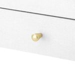 Close-up on gold cone-shaped knob with white washed lacquered linen texture on drawer front