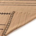 Corner of rug lifted to reveal tightly woven backside with faint linear pattern and overlock stitching