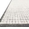 Angled side view highlighting pile texture and thick black striped border around the ivory rug