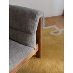 Close-up showing chair’s foldover back upholstery detail over wooden frame on yellow area rug