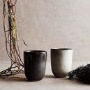 Two Mame Cups in black and white placed on a table with dried plants artfully arranged nearby