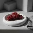Side view of tray holding a bunch of red grapes on a concrete surface with textured shadows