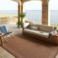 Rust rug styled on covered patio with wicker sofa, chair, and lake view in background