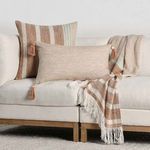 Decorative living room setting with pillow layered with tassel-trimmed beige lumbar pillow and matching throw blanket