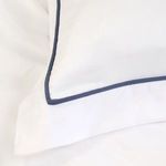Close-up of white bamboo sateen fabric with navy piping detail on duvet corner
