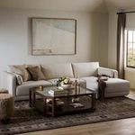 Styled room scene with sectional, decorative pillows, glass-top coffee table, and artwork above sofa