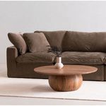 Close-up of wood coffee table with vase in front of dark brown sofa arm and cushions