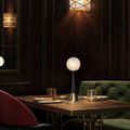 Table lamp on dark wood dining table with dark green velvet sofa and red chair background