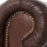 Close-up of rolled arm end with brass nailhead trim detail on leather Chesterfield sofa