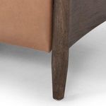 Close-up of wood frame leg in dark finish supporting warm brown leather chair