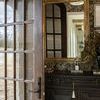 Mirror mounted on floral wallpapered wall near wooden glass panel door with black console below