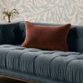 cinnamon pillow styled on blue tufted sofa with decorative wallpaper background