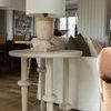 Lamp set on round wood side table with turned legs beside white couch in natural light living room