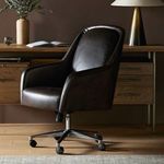 Verne chair shown in office setting with wooden desk, lamp, and wall background