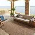 Merrick Oatmeal Multi rug styled outdoors on stone patio by wicker sofa with lake view