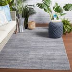 Gray-blue rug styled in outdoor space with wicker sofa, green plants, and decorative blue ottoman