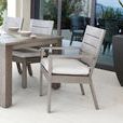 Outdoor dining setting featuring Laguna chairs with arms and cream cushions around a matching wood-textured table