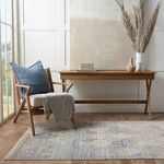 Blue pillow styled on beige cushioned chair next to wooden desk and dried pampas