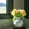 Cream reactive glaze vase displayed on marble corner countertop with patterned green wallpaper