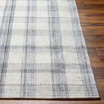 Top-down close detail of rug’s black and gray plaid weave and edge on wooden flooring