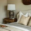 Bedroom corner with fall brown block print pillow on bed, wooden nightstand, ceramic lamp, and woven wall decoration