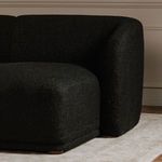 Close-up detail of textured black boucle fabric on sectional arm corner with wooden floor and baseboard