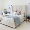 Wide view of bedroom with light pink pillows on bed featuring striped accent pillow and blue quilt