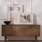 Turned pedestal bowl displayed on dark wooden cabinet with layered framed photos in softly lit interior