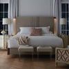 Dimly lit bedroom scene with king beige bed and blush accent pillows on herringbone wood floor