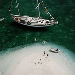 Zoomed-in portion highlighting the yacht hull, swimmer, and small boat with textured green water around the sandbar