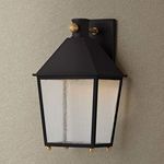 Gladden wall sconce mounted on textured beige wall showing warm illumination through seeded glass