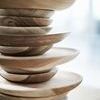 Close-up of stacked dinner plates showing rounded edges and natural wood texture in ambient light