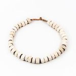 Circular arrangement of smaller faceted white cow bone beads with darker areas on the string ends