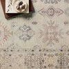 Close-up of rug pattern showing soft pink, blue, and beige detailed motifs with a book and small stones on corner