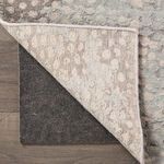 Dark gray rug pad placed under corner of patterned area rug on wood flooring, showing use context