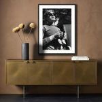 Framed Warhol photo hanging above vintage gold cabinet with dark wood floor and dried flowers in vase