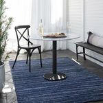 Rug on stone floor in outdoor dining space with round table, chairs, wine glasses