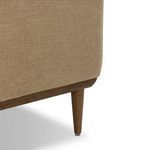 Close-up on tapered wood leg attached to rounded wood base with light tan upholstery