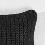 Close-up of chunky handwoven knit texture on corner of black outdoor throw pillow